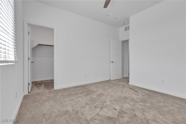 unfurnished bedroom featuring light carpet, ceiling fan, a walk in closet, and a closet