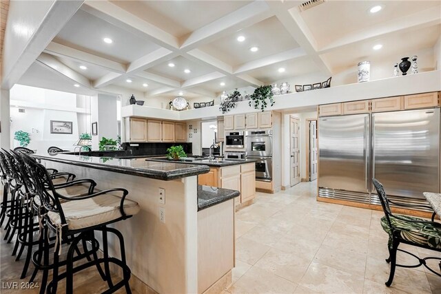 kitchen featuring light brown cabinetry, stainless steel appliances, dark stone counters, a breakfast bar area, and tasteful backsplash