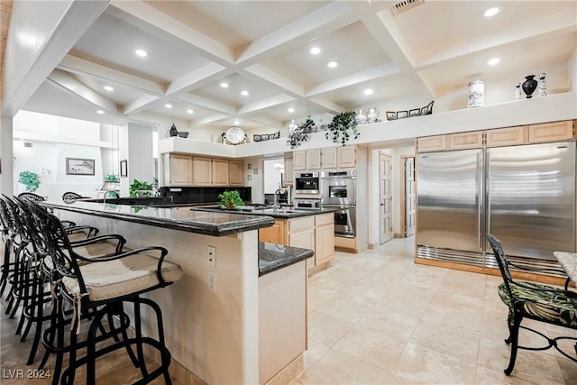 kitchen with coffered ceiling, a breakfast bar area, stainless steel appliances, light brown cabinetry, and a sink