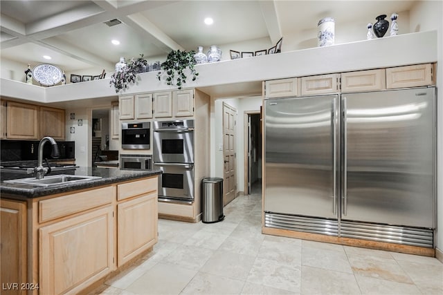 kitchen featuring light brown cabinetry, stainless steel appliances, beamed ceiling, sink, and a kitchen island with sink