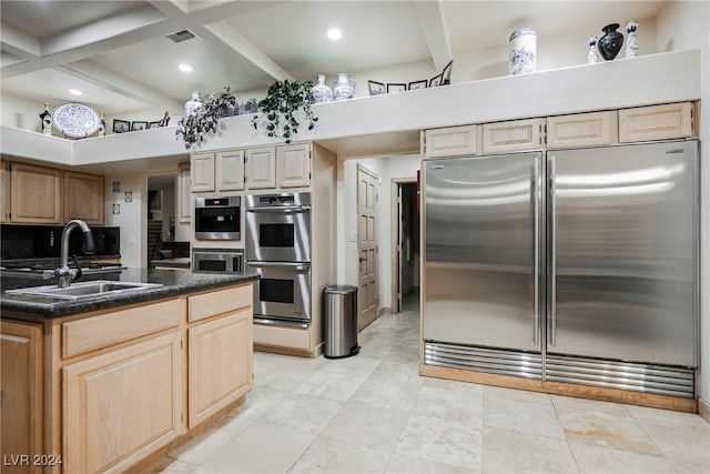 kitchen with stainless steel appliances, coffered ceiling, a sink, beamed ceiling, and dark countertops