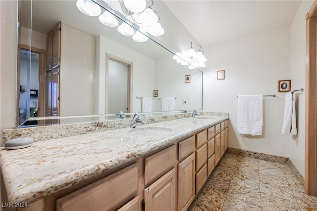 full bath featuring baseboards, a sink, an inviting chandelier, and double vanity