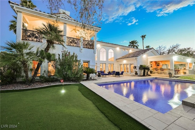 rear view of house with an outdoor pool, a balcony, french doors, a patio area, and stucco siding