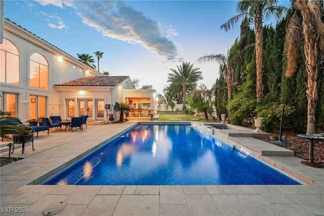 pool at dusk featuring pool water feature, a patio, and french doors