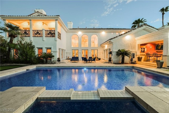 back of house featuring a patio, a chimney, a pool with connected hot tub, ceiling fan, and a balcony