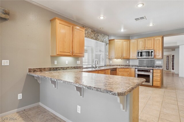 kitchen with light brown cabinets, a breakfast bar area, stainless steel appliances, and kitchen peninsula