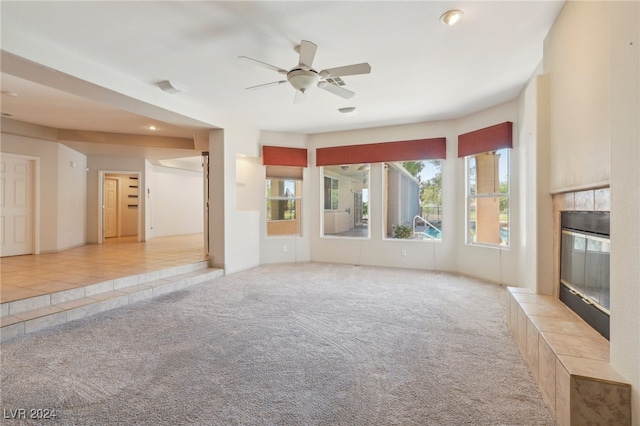 unfurnished living room with ceiling fan, light colored carpet, and a tile fireplace