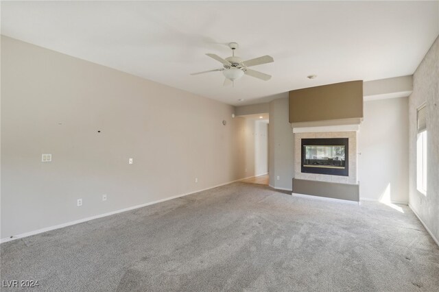 unfurnished living room featuring a multi sided fireplace, ceiling fan, and light colored carpet