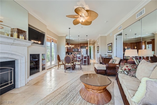 living area with crown molding, light tile patterned floors, ceiling fan with notable chandelier, visible vents, and a glass covered fireplace