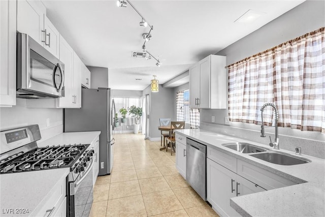 kitchen with appliances with stainless steel finishes, rail lighting, sink, light tile patterned floors, and white cabinets