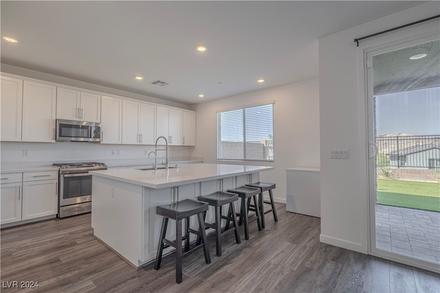 kitchen with a kitchen bar, appliances with stainless steel finishes, a center island with sink, white cabinets, and dark hardwood / wood-style floors