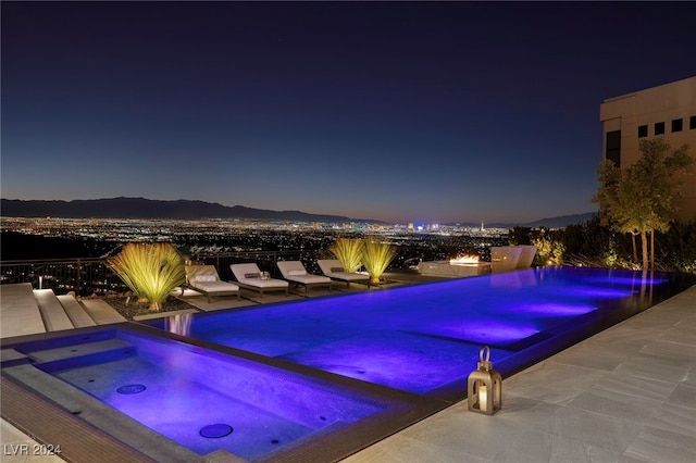 pool at twilight featuring a patio, a mountain view, and an in ground hot tub