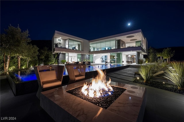 back house at night featuring a balcony, an outdoor fire pit, and a patio area