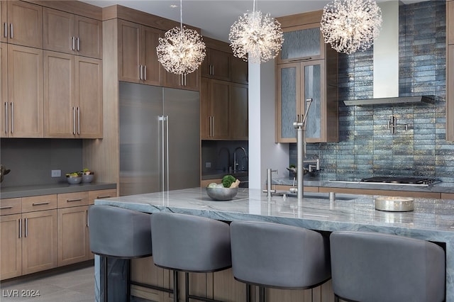 kitchen featuring wall chimney exhaust hood, built in fridge, a kitchen bar, pendant lighting, and tasteful backsplash