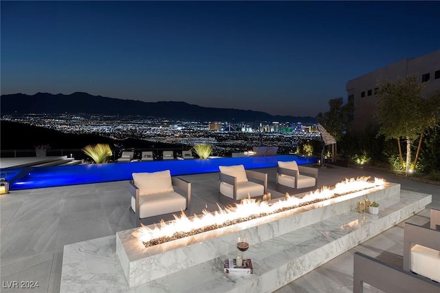 pool at night with an infinity pool, a patio area, and a mountain view