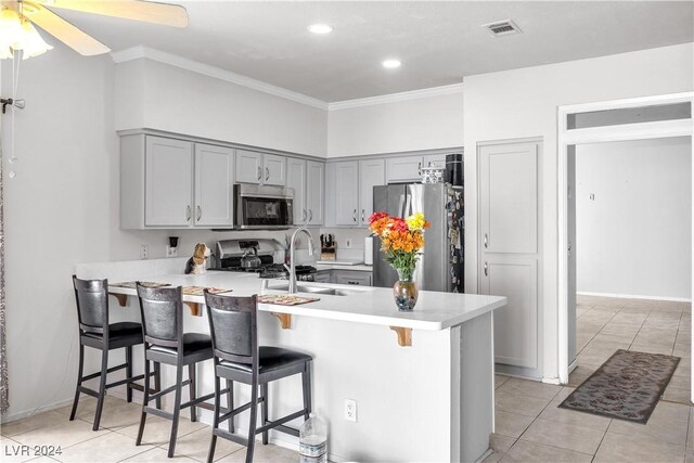 kitchen featuring ceiling fan, ornamental molding, kitchen peninsula, stainless steel appliances, and a kitchen breakfast bar