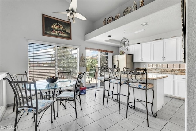 kitchen with stainless steel fridge, white cabinetry, ceiling fan, light stone counters, and light tile patterned flooring