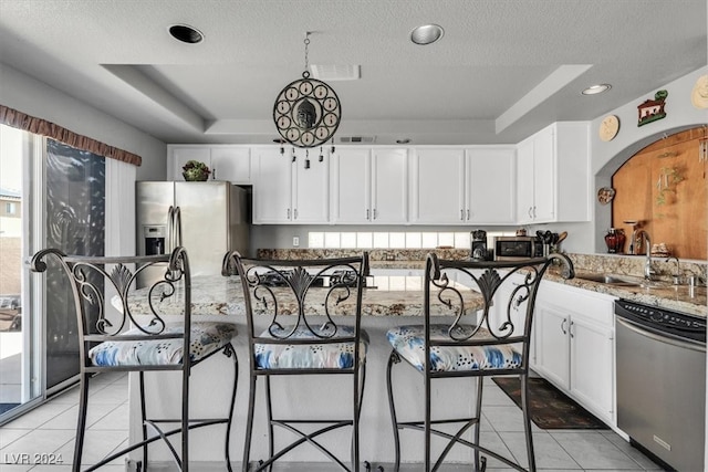 kitchen with a raised ceiling, dark stone countertops, a breakfast bar, and appliances with stainless steel finishes