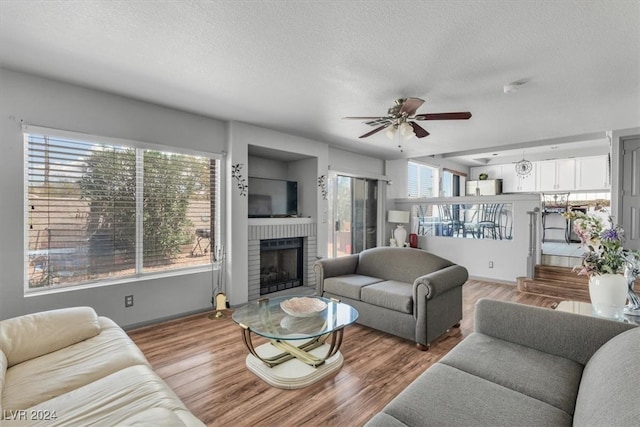 living room with a fireplace, a textured ceiling, wood-type flooring, and ceiling fan