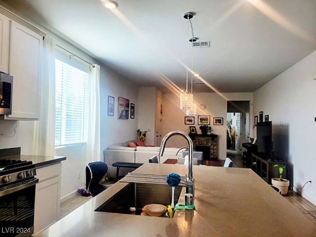 kitchen with decorative light fixtures, a fireplace, stainless steel appliances, hardwood / wood-style flooring, and white cabinets