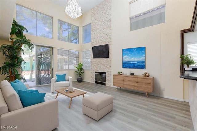 living room featuring a high ceiling, a stone fireplace, wood finished floors, a chandelier, and baseboards