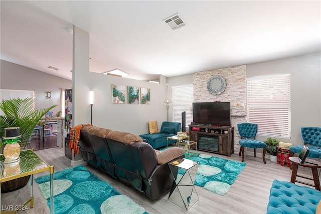 living room featuring light wood-type flooring, lofted ceiling, and a stone fireplace