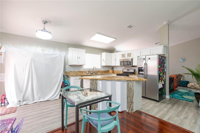 kitchen with white cabinets, light hardwood / wood-style flooring, appliances with stainless steel finishes, light stone counters, and a kitchen island