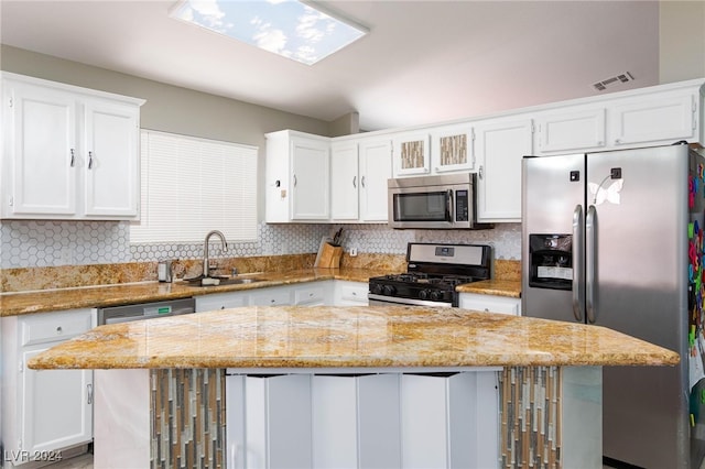 kitchen featuring white cabinets, a center island, light stone counters, stainless steel appliances, and sink