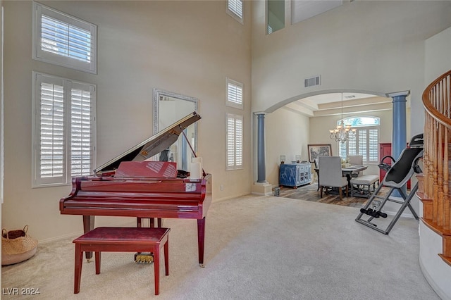 misc room featuring carpet, decorative columns, a chandelier, and a towering ceiling