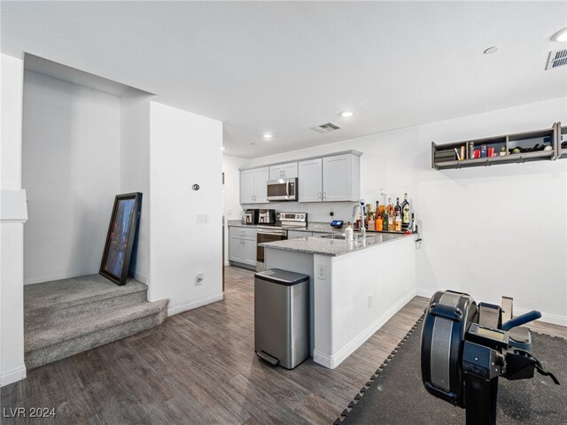 kitchen with appliances with stainless steel finishes, dark hardwood / wood-style flooring, light stone counters, and kitchen peninsula