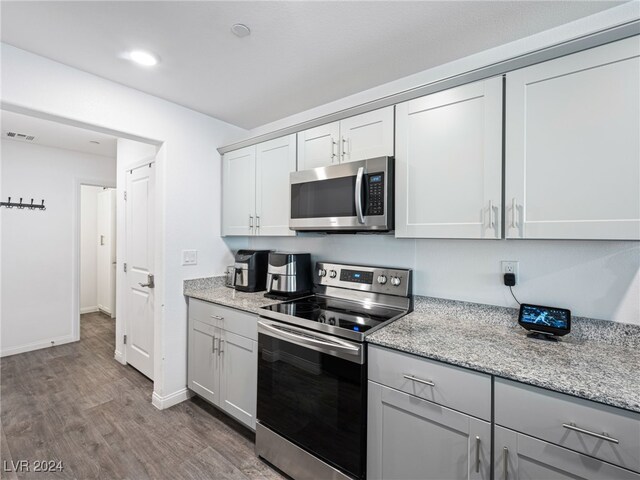 kitchen with appliances with stainless steel finishes, light stone counters, white cabinets, and dark hardwood / wood-style floors