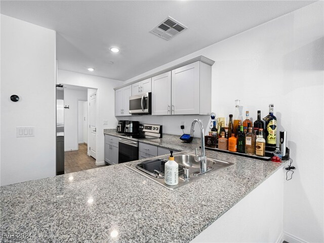 kitchen with light stone counters, kitchen peninsula, sink, appliances with stainless steel finishes, and light hardwood / wood-style floors