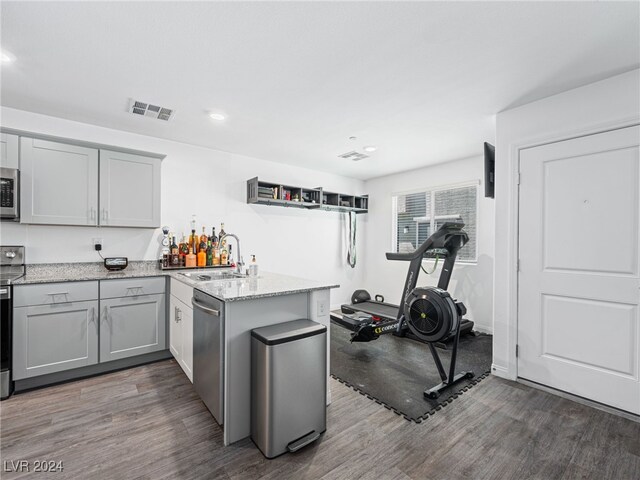 kitchen featuring stainless steel appliances, dark hardwood / wood-style flooring, kitchen peninsula, sink, and light stone countertops