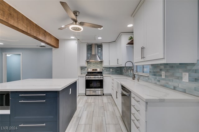 kitchen featuring stainless steel appliances, wall chimney exhaust hood, backsplash, light stone countertops, and white cabinetry