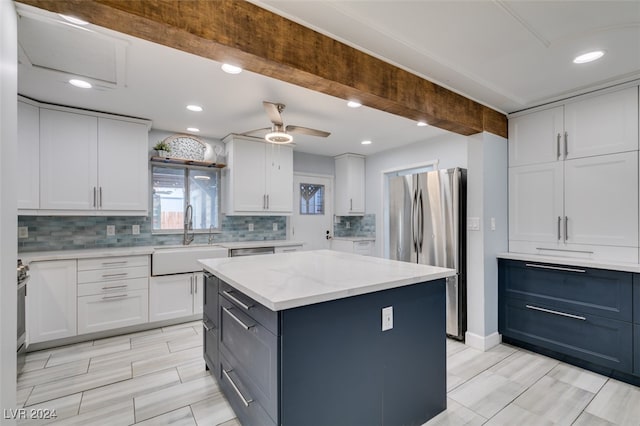 kitchen featuring stainless steel refrigerator, white cabinetry, sink, and a center island