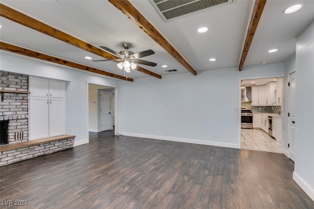 unfurnished living room featuring ceiling fan, beamed ceiling, light wood-type flooring, and a brick fireplace