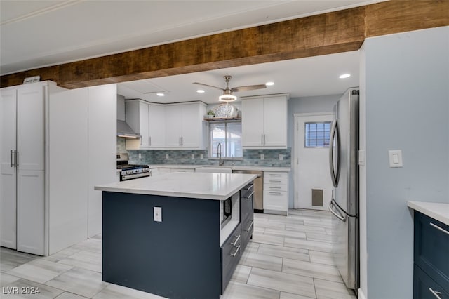 kitchen with stainless steel appliances, a center island, white cabinets, decorative backsplash, and wall chimney range hood