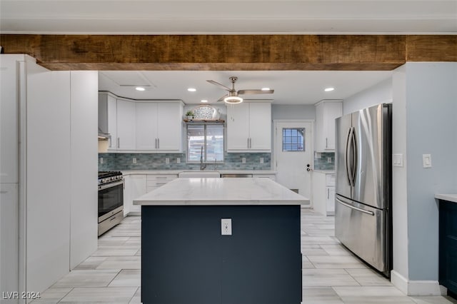 kitchen with stainless steel appliances, beamed ceiling, white cabinetry, light stone countertops, and a center island