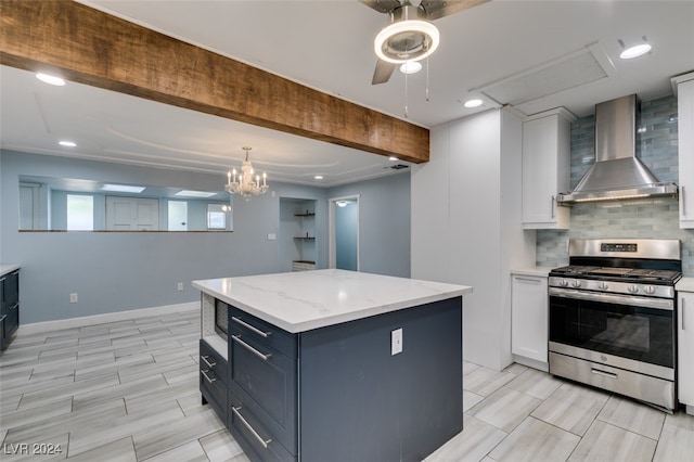 kitchen featuring a kitchen island, white cabinets, wall chimney range hood, stainless steel gas stove, and decorative backsplash