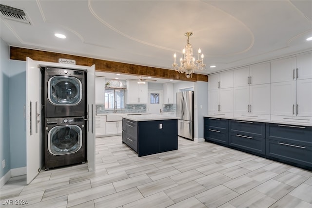 kitchen featuring a chandelier, a kitchen island, stainless steel refrigerator, white cabinetry, and stacked washer and dryer