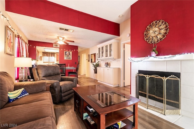 living room featuring a textured ceiling, ceiling fan, hardwood / wood-style floors, and a tile fireplace