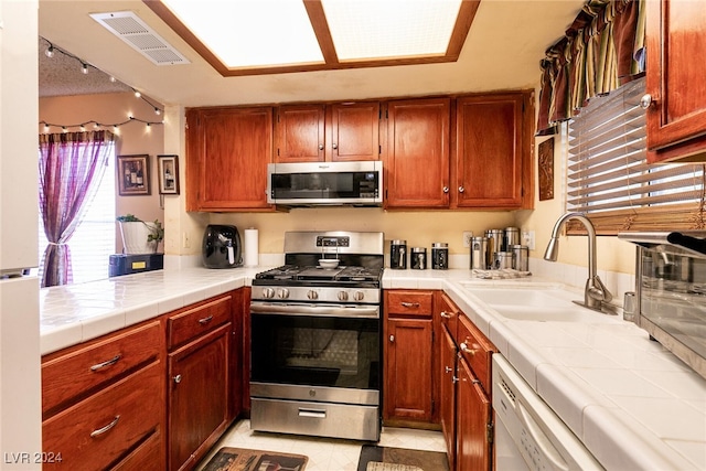 kitchen featuring appliances with stainless steel finishes, light tile patterned floors, tile counters, and sink