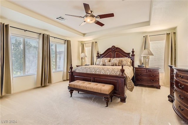 bedroom with light carpet, a tray ceiling, and ceiling fan