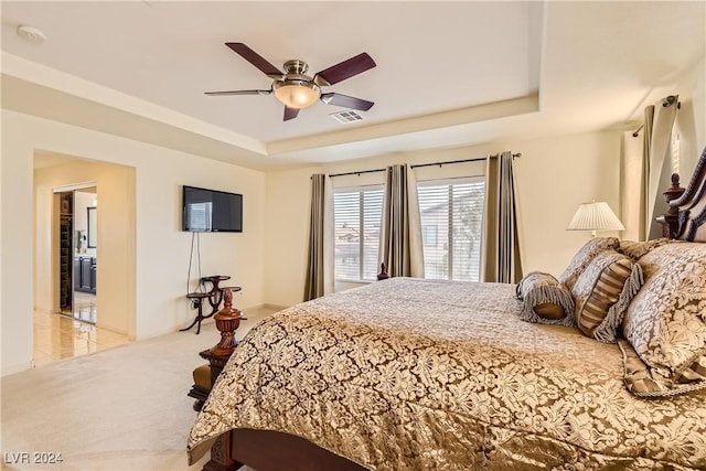 carpeted bedroom with a raised ceiling and ceiling fan