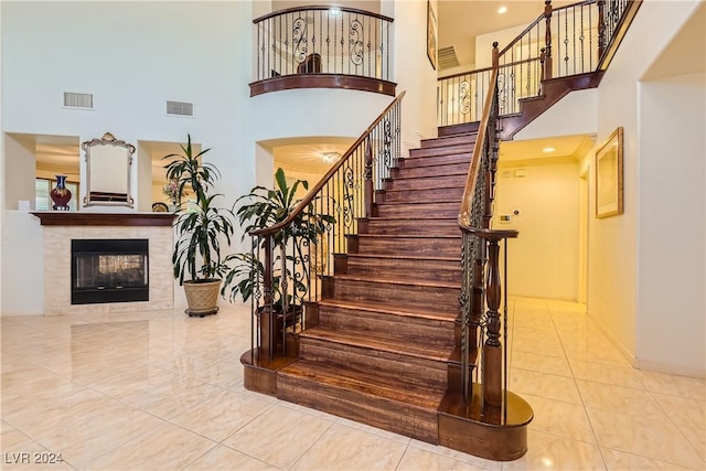 stairway featuring tile patterned flooring, a towering ceiling, and a tile fireplace