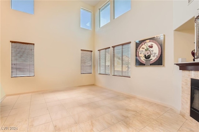 unfurnished living room with a tile fireplace, a towering ceiling, plenty of natural light, and light tile patterned flooring