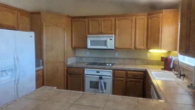 kitchen featuring tile counters, sink, light tile patterned floors, and white appliances