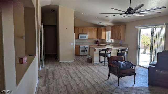 kitchen featuring kitchen peninsula, lofted ceiling, a breakfast bar, light hardwood / wood-style floors, and white appliances