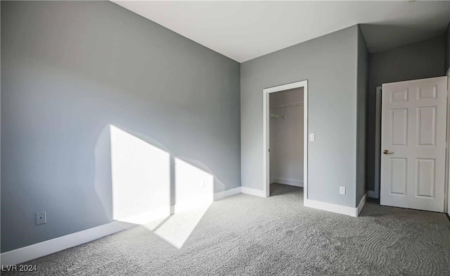 unfurnished bedroom with a walk in closet, dark colored carpet, and a closet