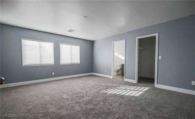 unfurnished bedroom featuring a closet, a walk in closet, carpet, and ensuite bath